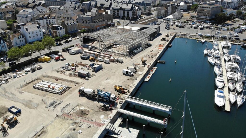 Vue d’ensemble aérienne du chantier portuaire de Saint-Malo, avec le bâtiment en construction, les fondations, les quais et les bateaux amarrés dans le bassin.