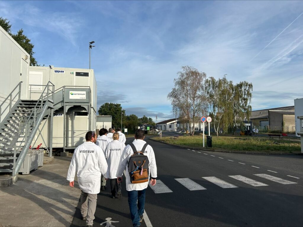 Groupe de visiteurs se déplaçant dans les espaces extérieurs du site ARMOR-IIMAK, entre les bâtiments et les installations industrielles.