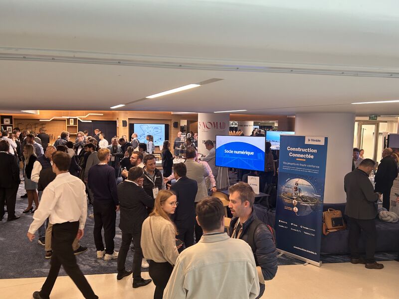Vue de l’espace exposants, où les participants discutent entre les stands et les écrans de présentation. Les supports visibles mettent notamment en avant le socle numérique et la construction connectée.